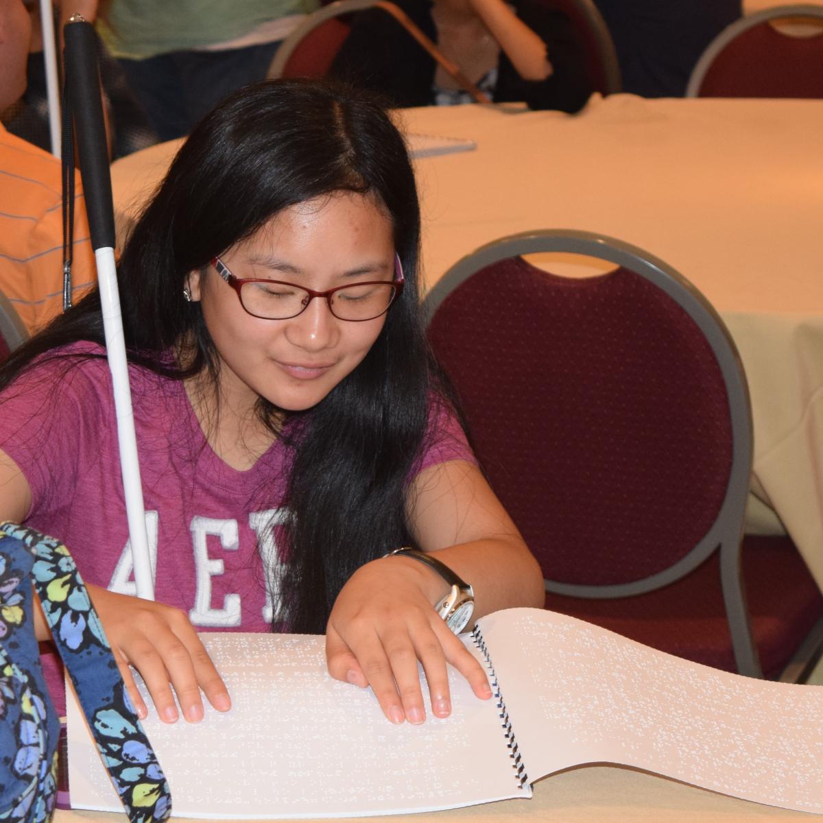 a teen girl reading braille at a table.