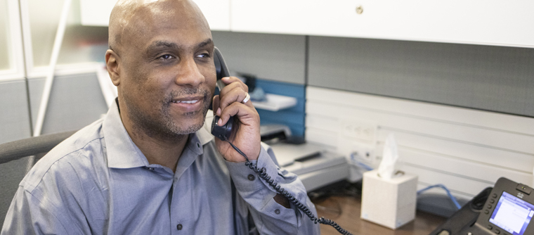 A man smiles while he listens to a telephone receiver.